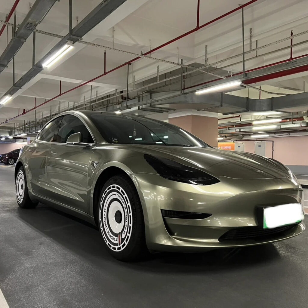 Olive Tesla Model 3 with custom white wheel covers parked in an underground garage