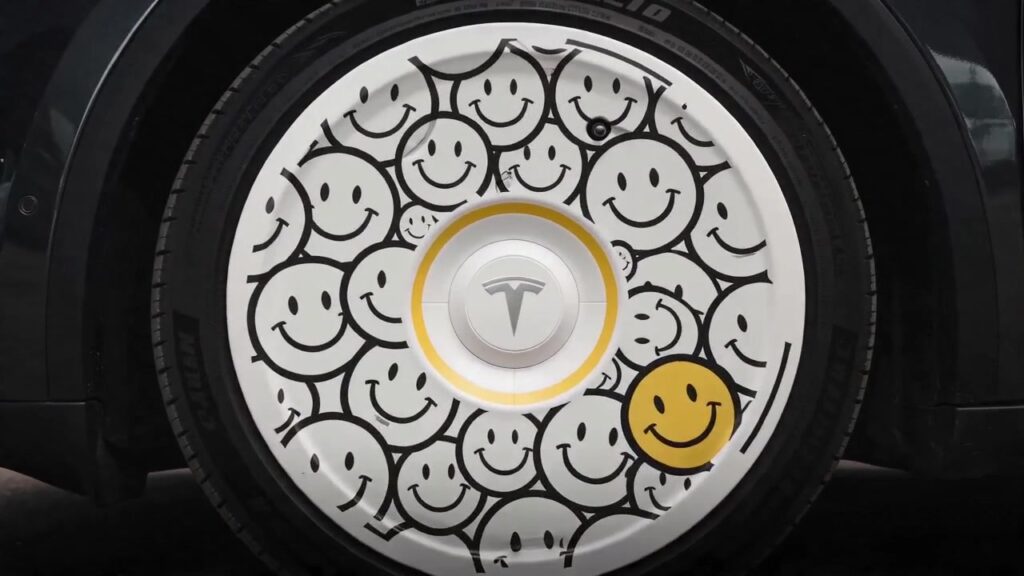 Custom painted Tesla wheel cover with smiley face design on a dark Model Y